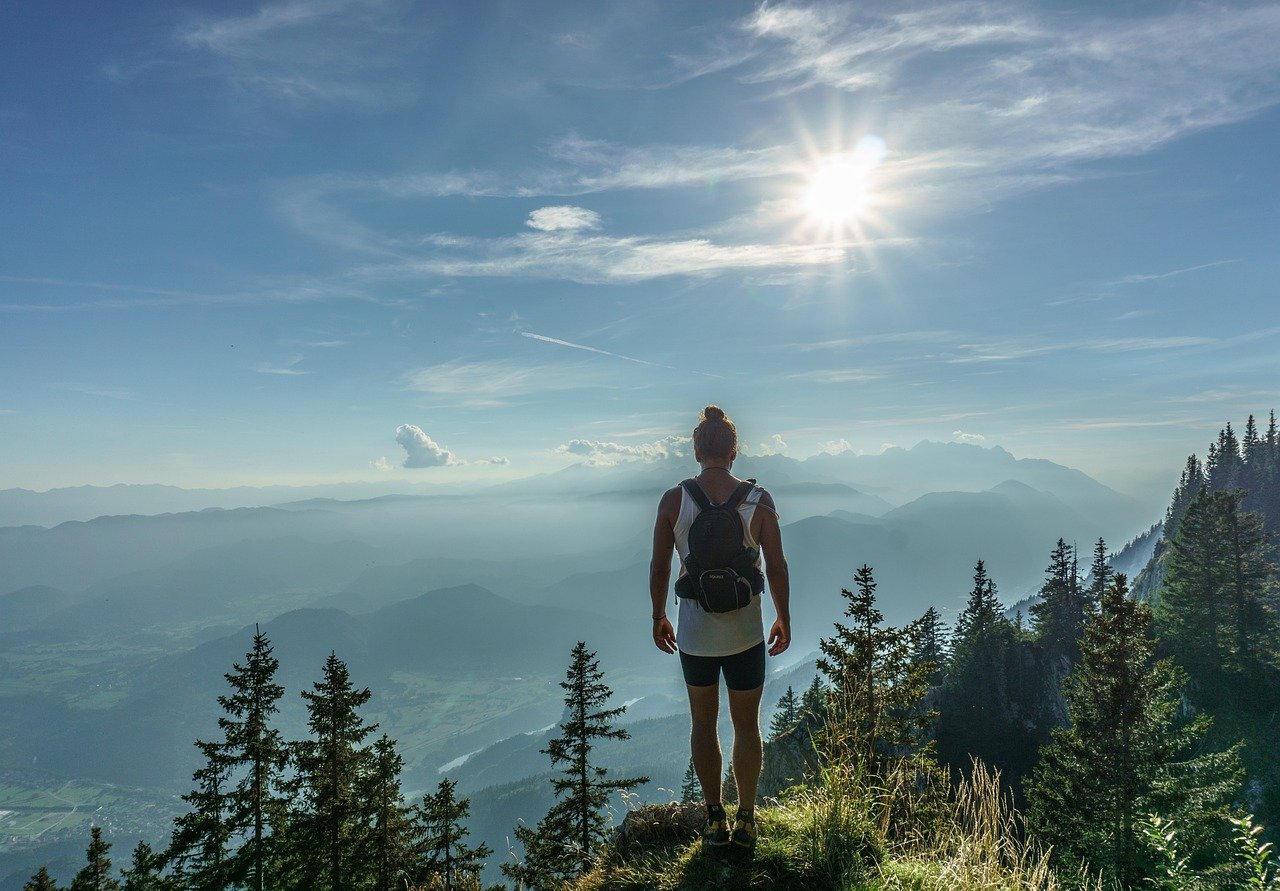 A solo traveler with a backpack standing on a cliff overlooking a South American landscape with mountains and a river.
