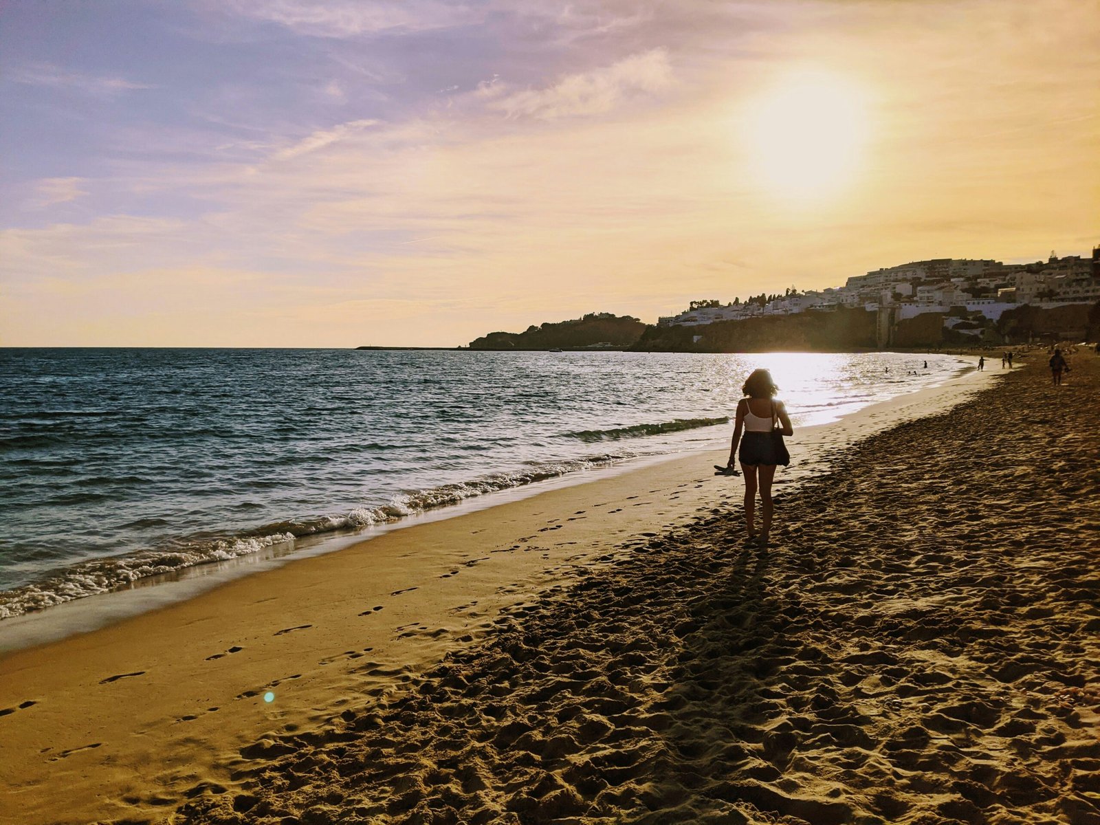 A traveler walking along a coastal path in Cadaqués, Spain, with the Mediterranean Sea sparkling in the background.