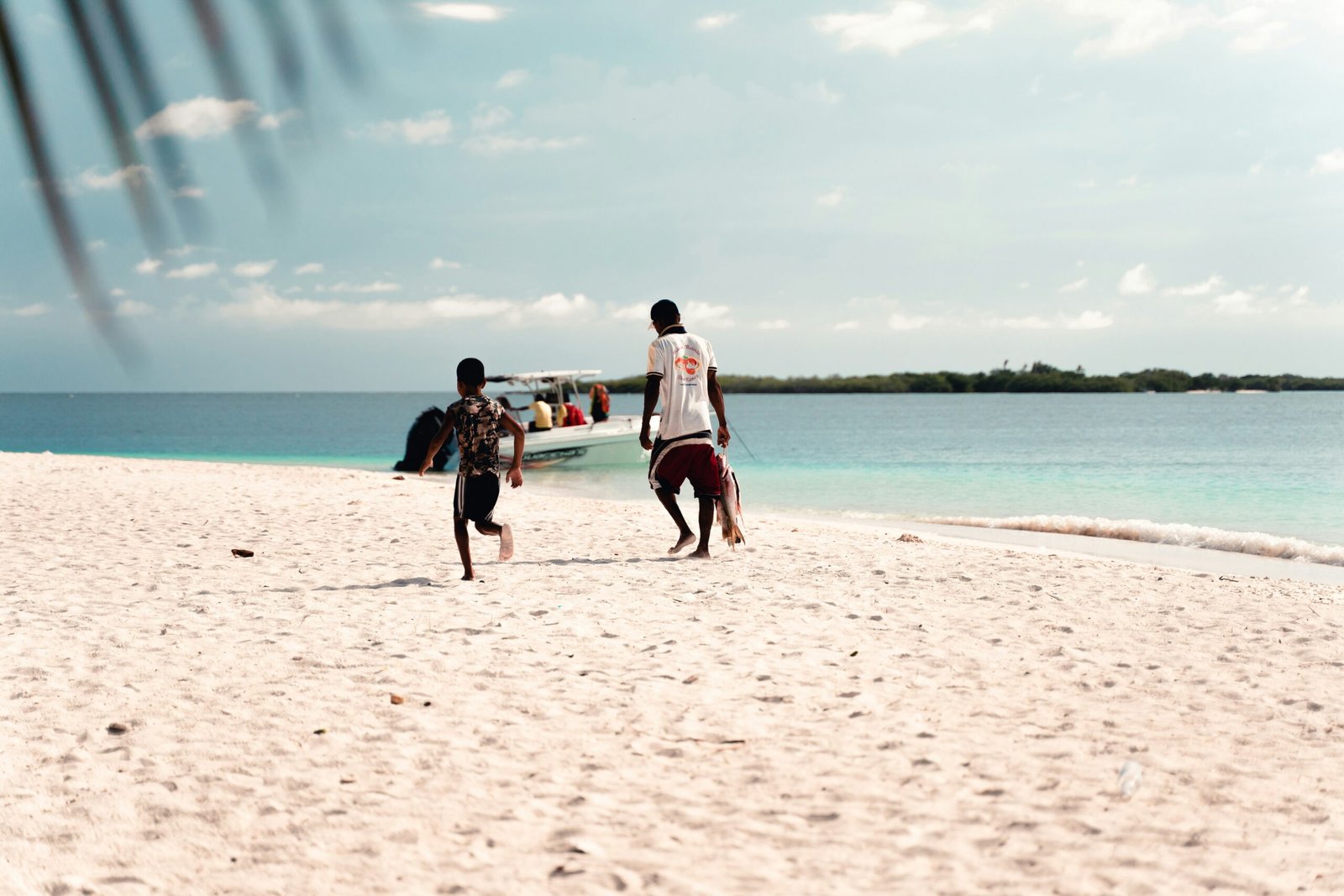 A family playing on a white-sand beach in Fiji, with turquoise waters and palm trees in the background.