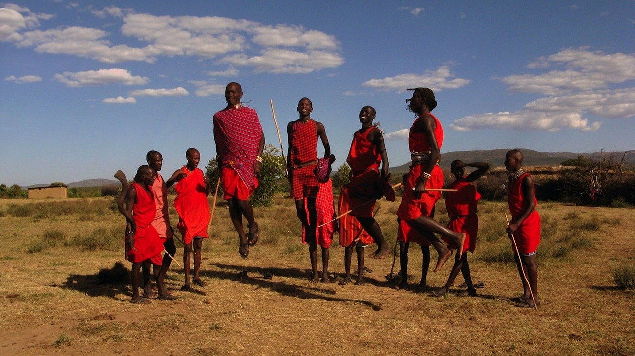 Maasai warriors in traditional red clothing performing a jumping dance in their village.