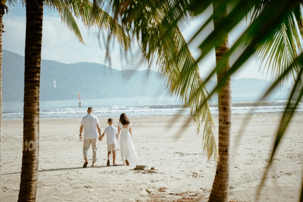 A family walking along a pristine beach in Oceania with turquoise waters and palm trees in the background.