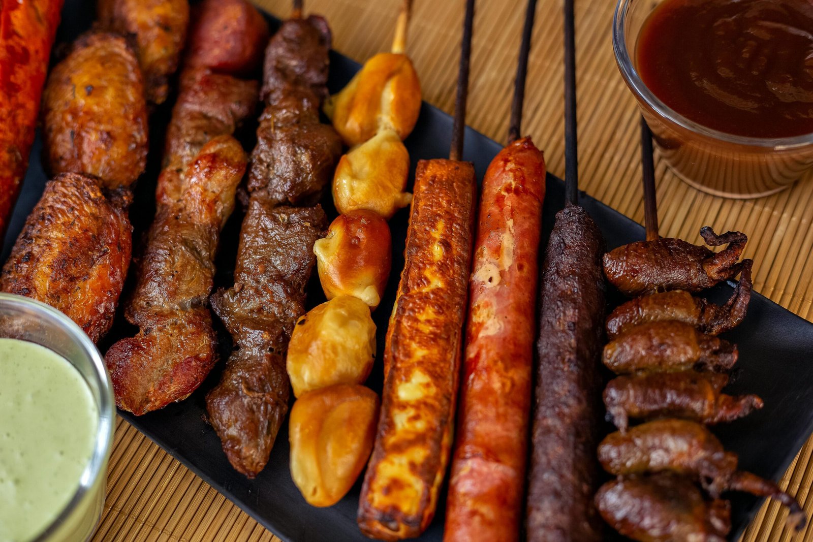 Mouthwatering variety of grilled meat skewers served on a black plate with sauces.