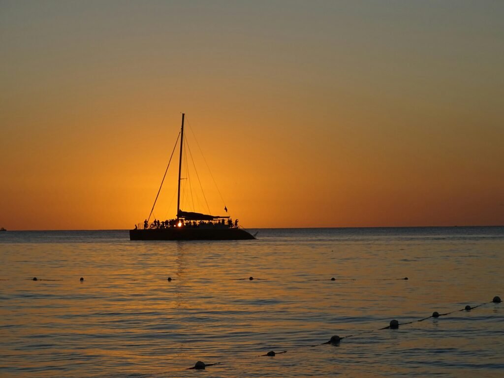Experience a tranquil sunset sail in Negril, Jamaica, silhouetted against a vibrant sky.