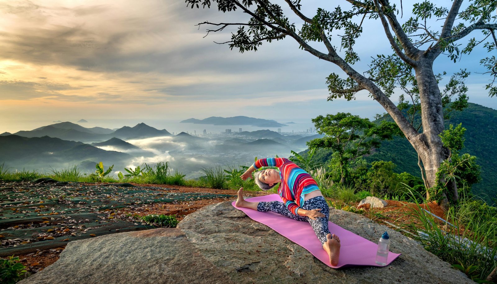 A senior woman performs yoga stretches on a mountain at sunrise, embracing a healthy outdoor lifestyle.