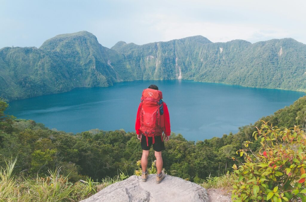 Hiker with backpack enjoying scenic mountain lake view on a bright summer day.