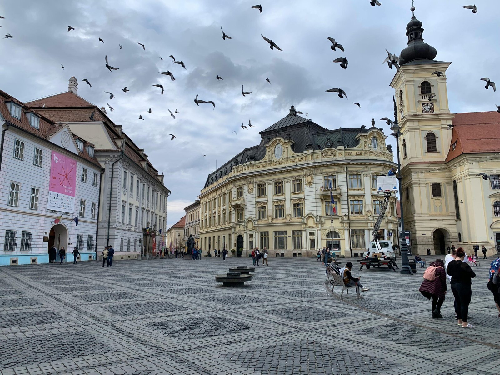 Lively square in Sibiu, Romania, with historic architecture and flying birds.