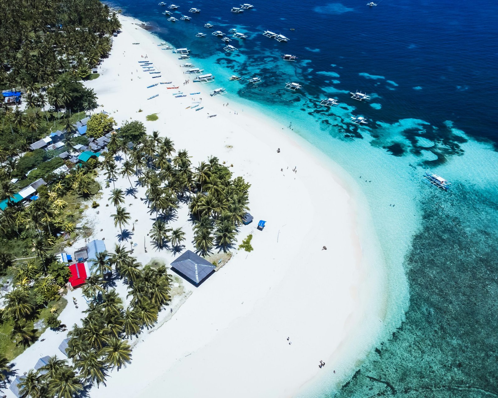 An aerial shot of a wooden boardwalk leading to a diving platform in the stunningly clear, turquoise water of Sugba Lagoon, Siargao.