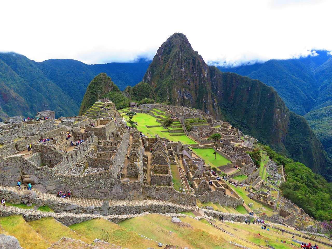 A classic, breathtaking view of Machu Picchu at sunrise, with the iconic Huayna Picchu mountain in the background and soft clouds in the valley.