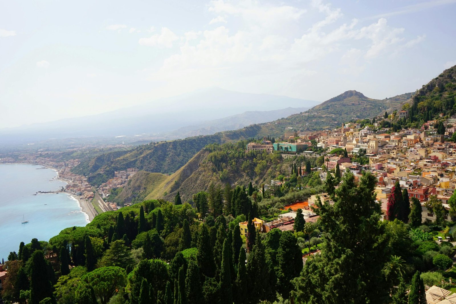 A breathtaking view of Taormina, Sicily with lush greenery, coastline, and hills under a summer sky.