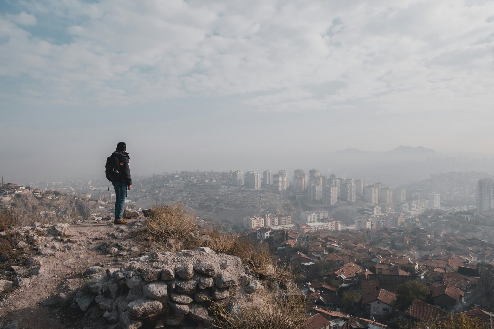 A confident-looking solo traveler standing on a scenic viewpoint overlooking a city, appearing aware of their surroundings but relaxed and empowered.