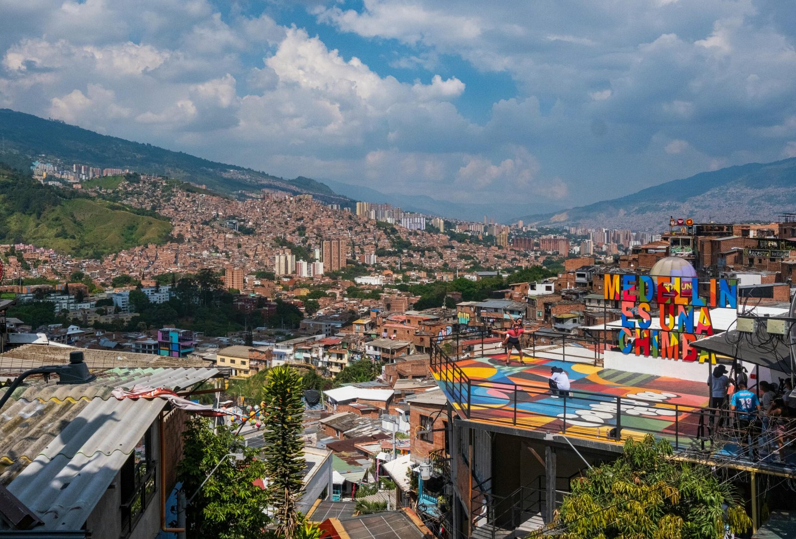 A vibrant, colorful street in the Comuna 13 neighborhood of Medellín, Colombia, with street art and people enjoying the day.