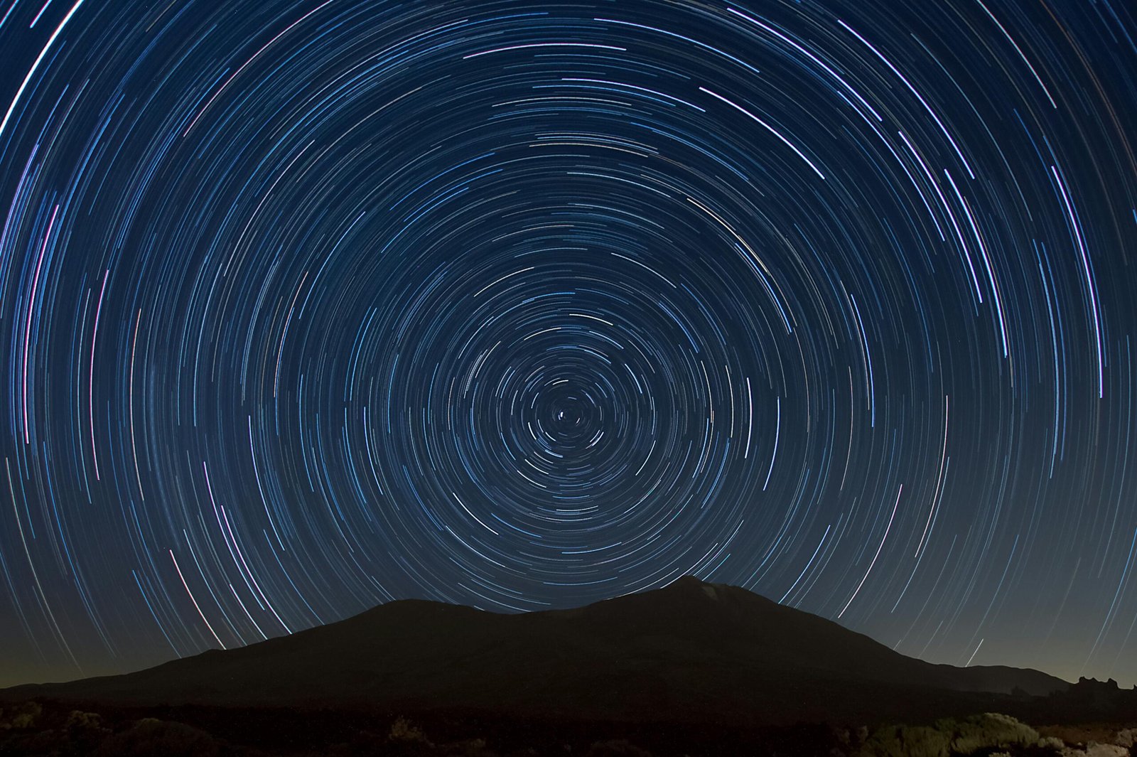 The volcanic caldera of Teide National Park in Tenerife at twilight, with the peak of Mount Teide and the observatory domes visible against a darkening, star-filled sky.