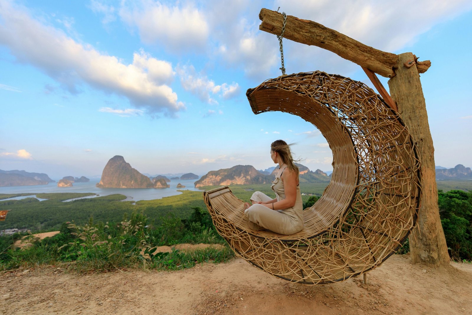 Woman in rattan hammock enjoying Phang-nga Bay's scenic view at sunset.